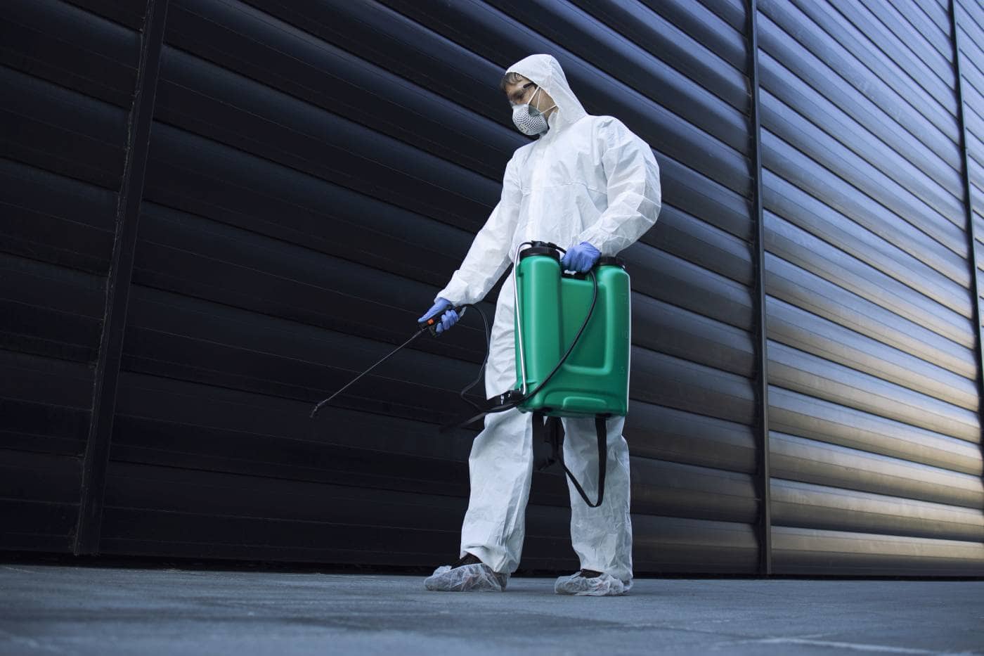 person in white chemical protection suit doing disinfection of public areas to stop spreading highly contagious corona virus.